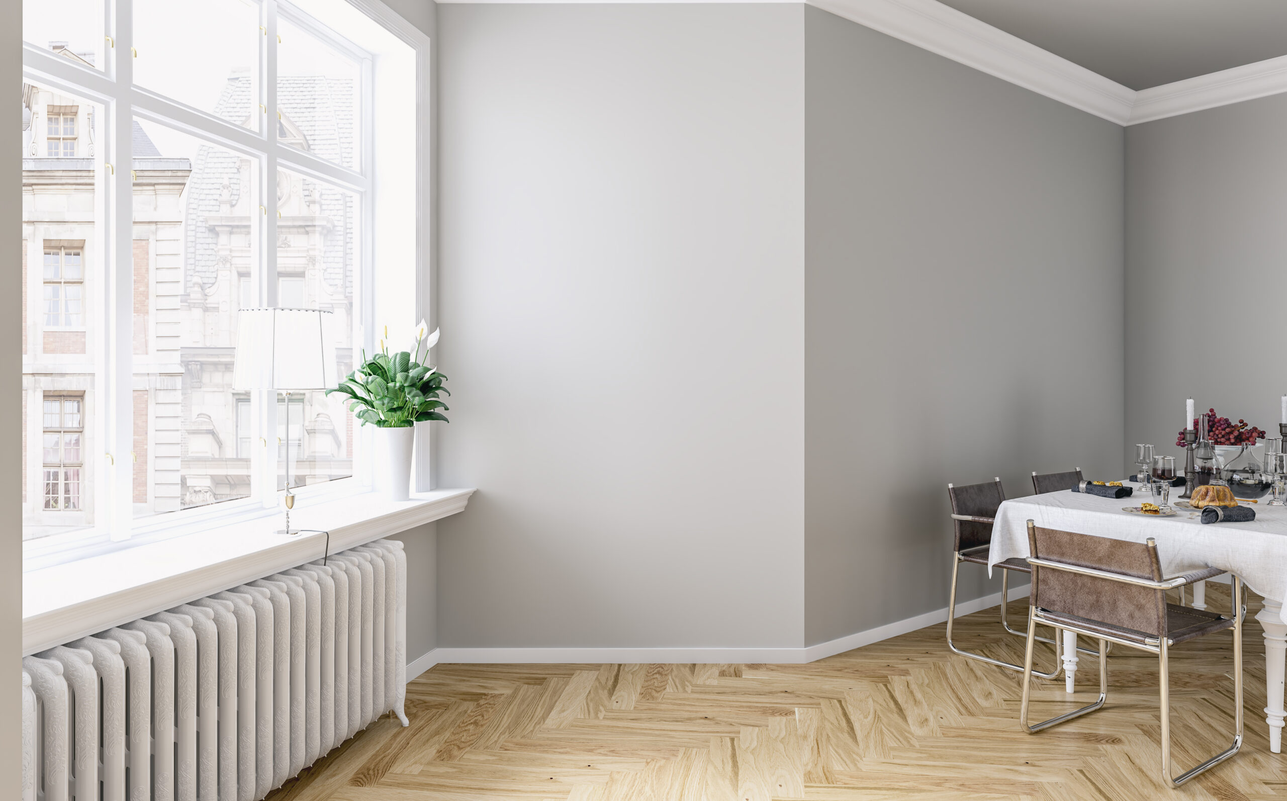 Un comedor moderno y bien iluminado con una gran ventana que deja entrar abundante luz natural. La mesa está preparada para una comida con mantelería blanca, copas y velas. El suelo es de parquet claro, y hay una planta decorativa junto a la ventana. La imagen ilustra la comodidad y estilo de un piso disponible para alquilar a través de una inmobiliaria.