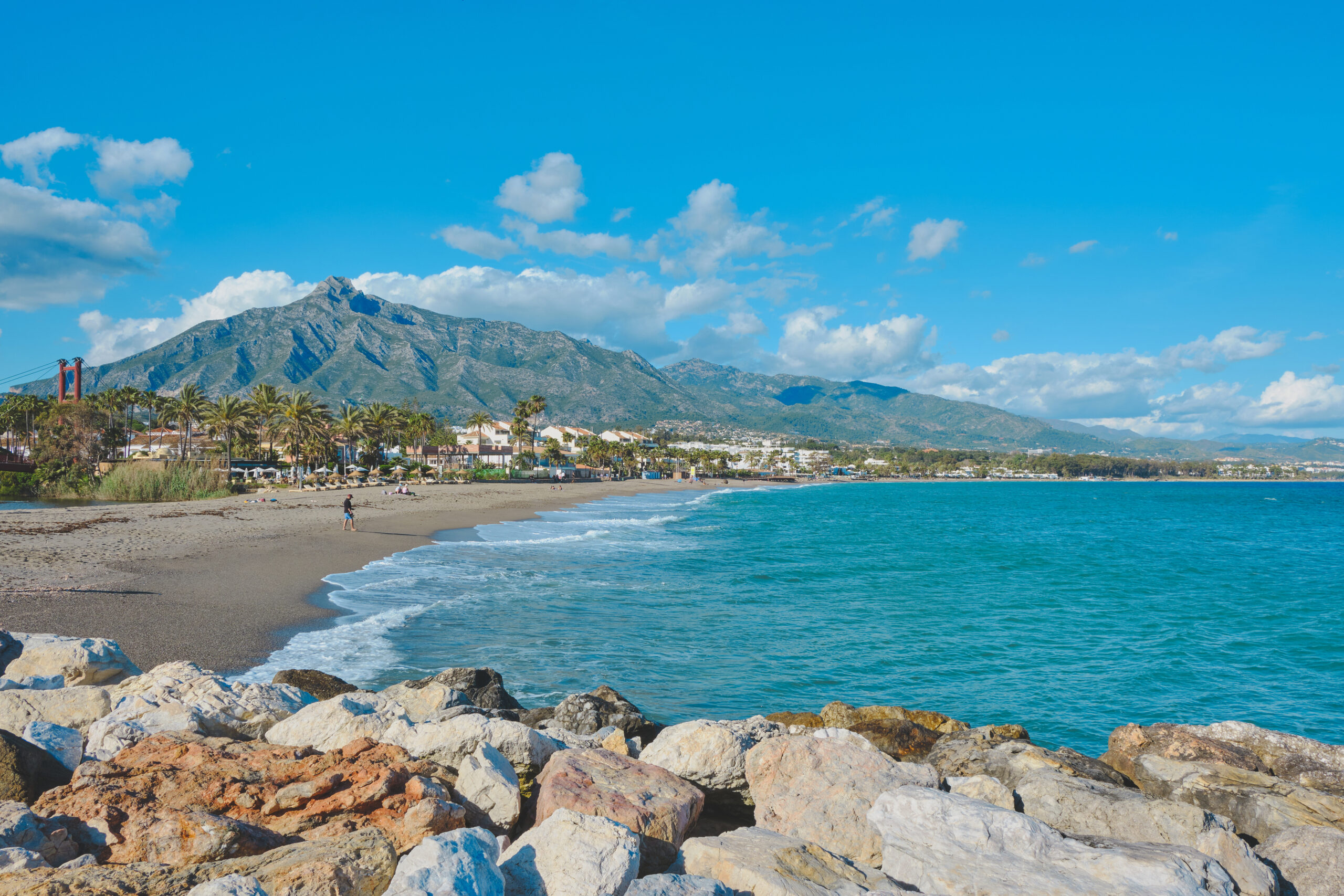 Vista panorámica de la playa en Marbella con montañas al fondo y un cielo despejado.