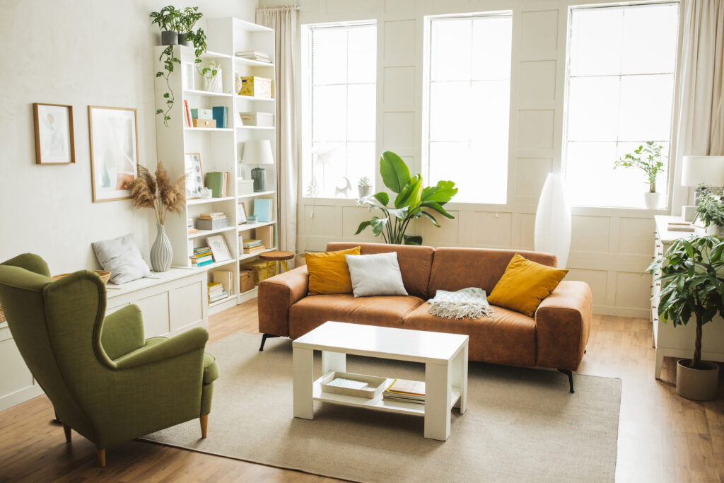 Sala de estar acogedora y bien iluminada con sofá de cuero marrón, sillón verde y estanterías llenas de libros.