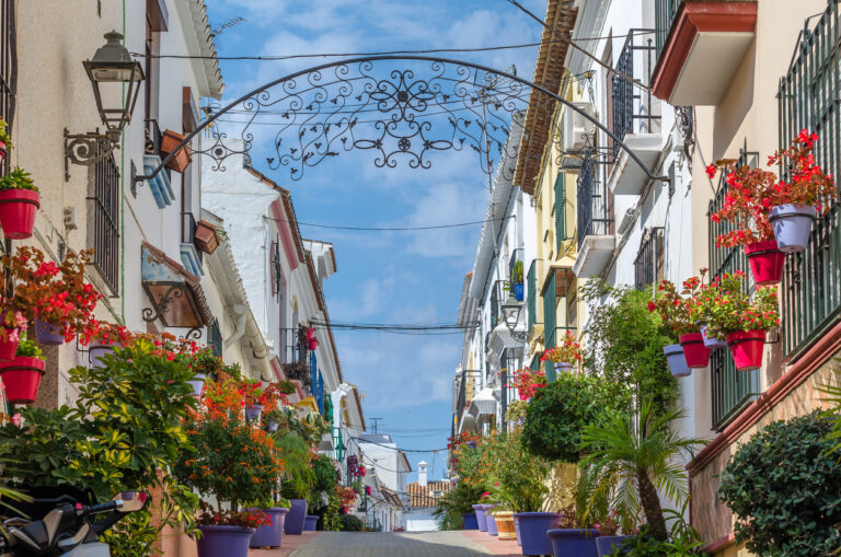 Calle típica de Estepona adornada con macetas de flores coloridas y arquitectura tradicional andaluza bajo un cielo azul.