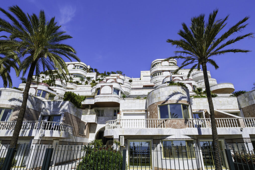 Lujosa vivienda en Puerto Banús con diseño arquitectónico moderno, rodeada de palmeras y bajo un cielo azul brillante.